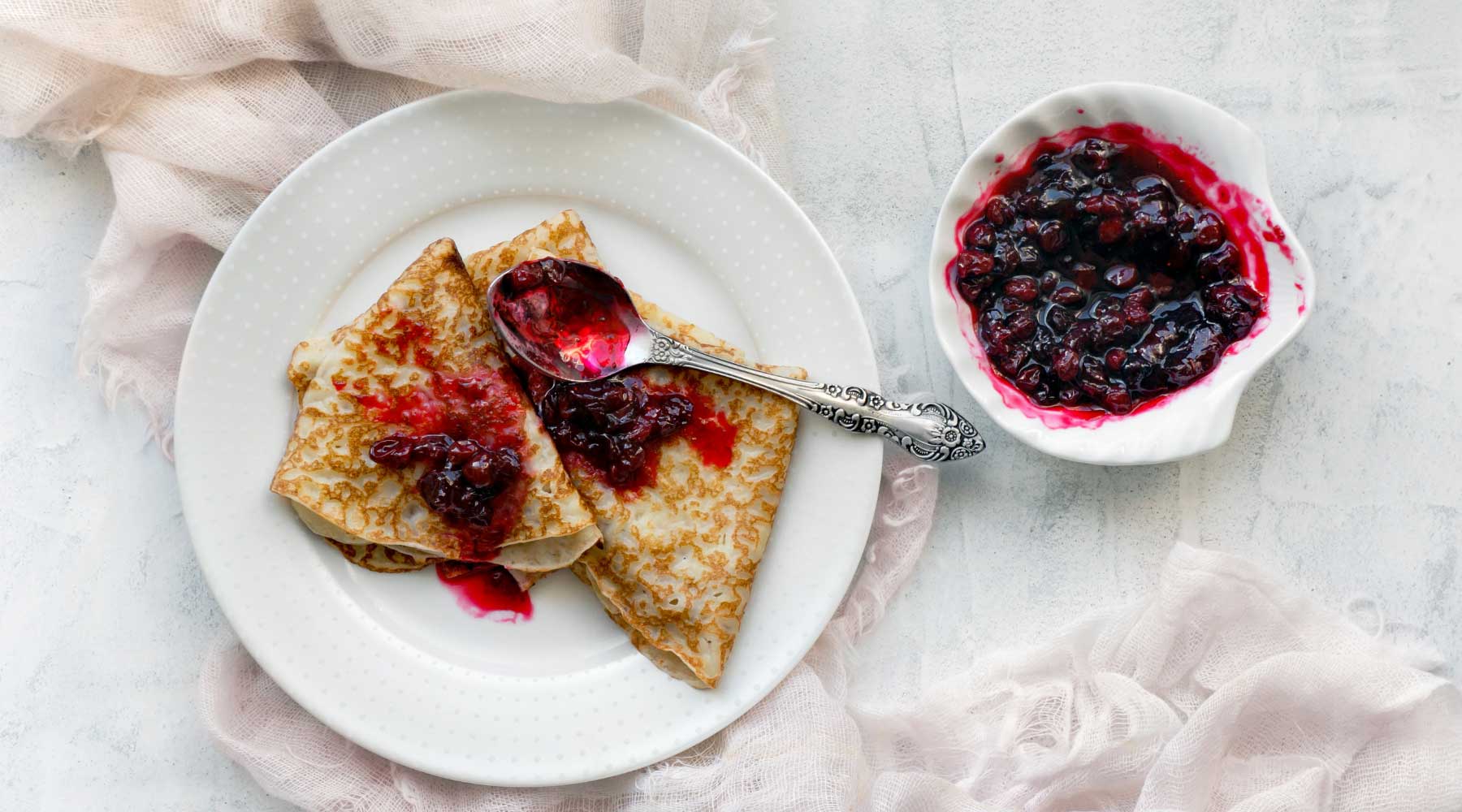Bowl with fruit jam and folded European crepes covered with jam