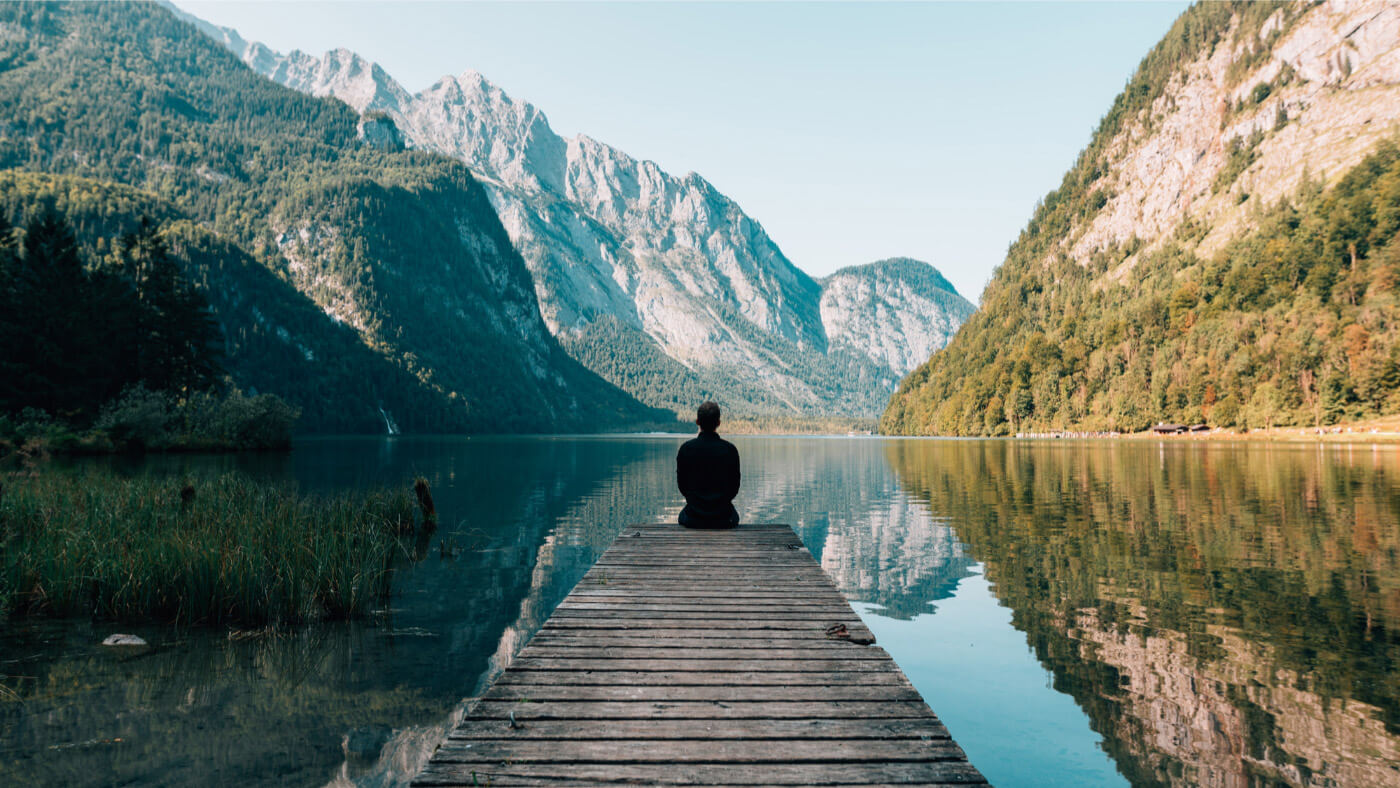 Man meditating on lake shore near mountains