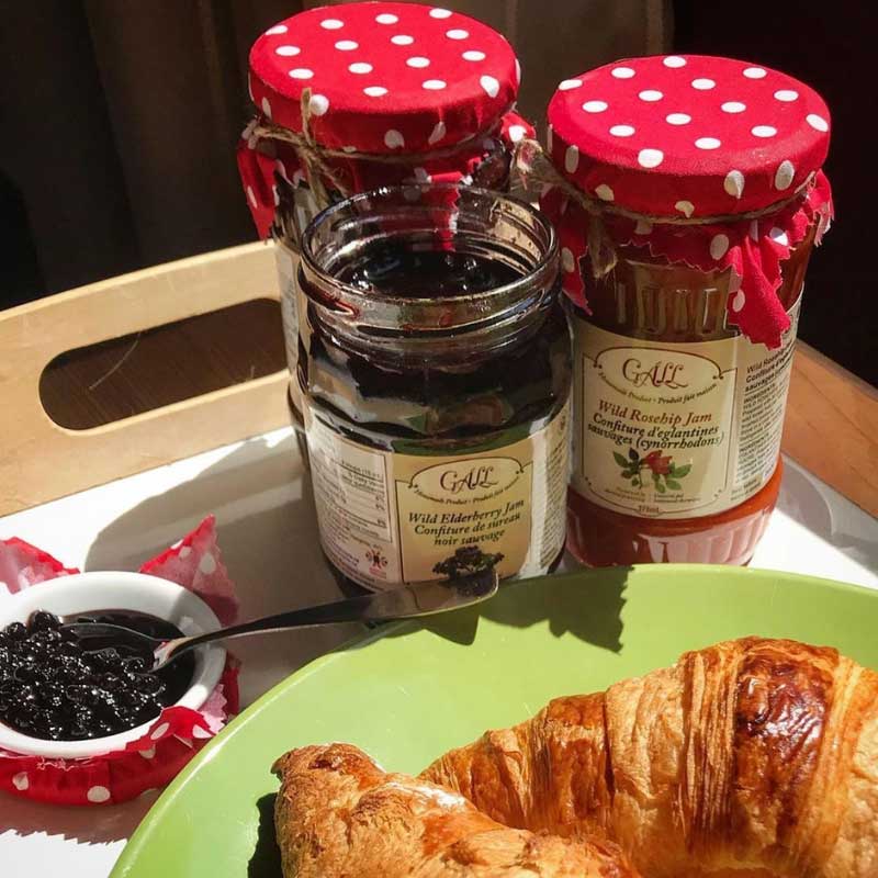 Croissants on green plate and small bowl with elderberry jam, near jars of Health from Europe jam - rosehip, elderberry, rose petal