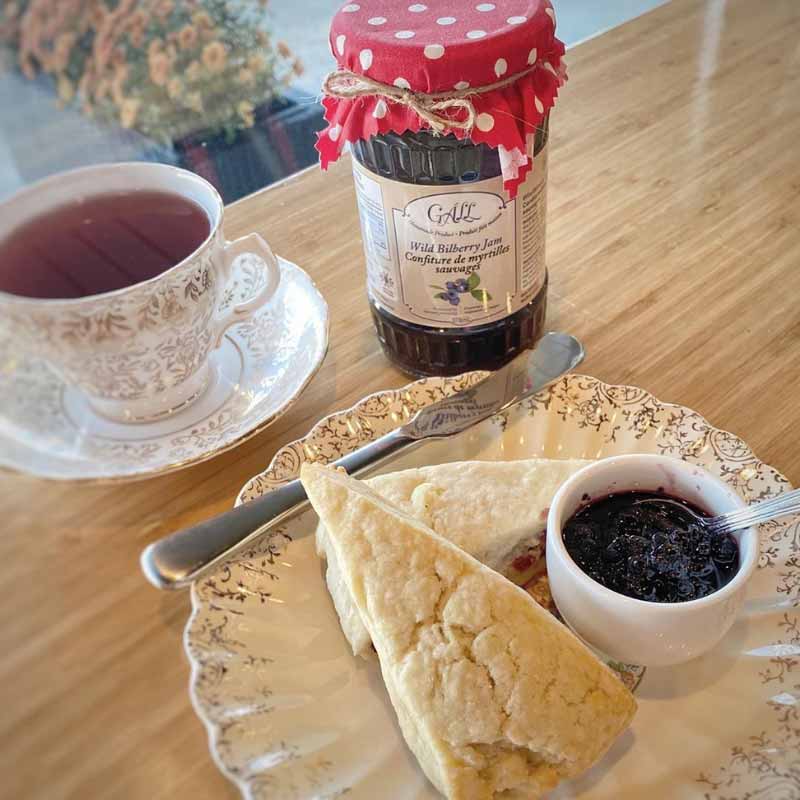 Cup of herbal tea, jar of Health from Europe bilberry jam, scones and bowl of jam on plate