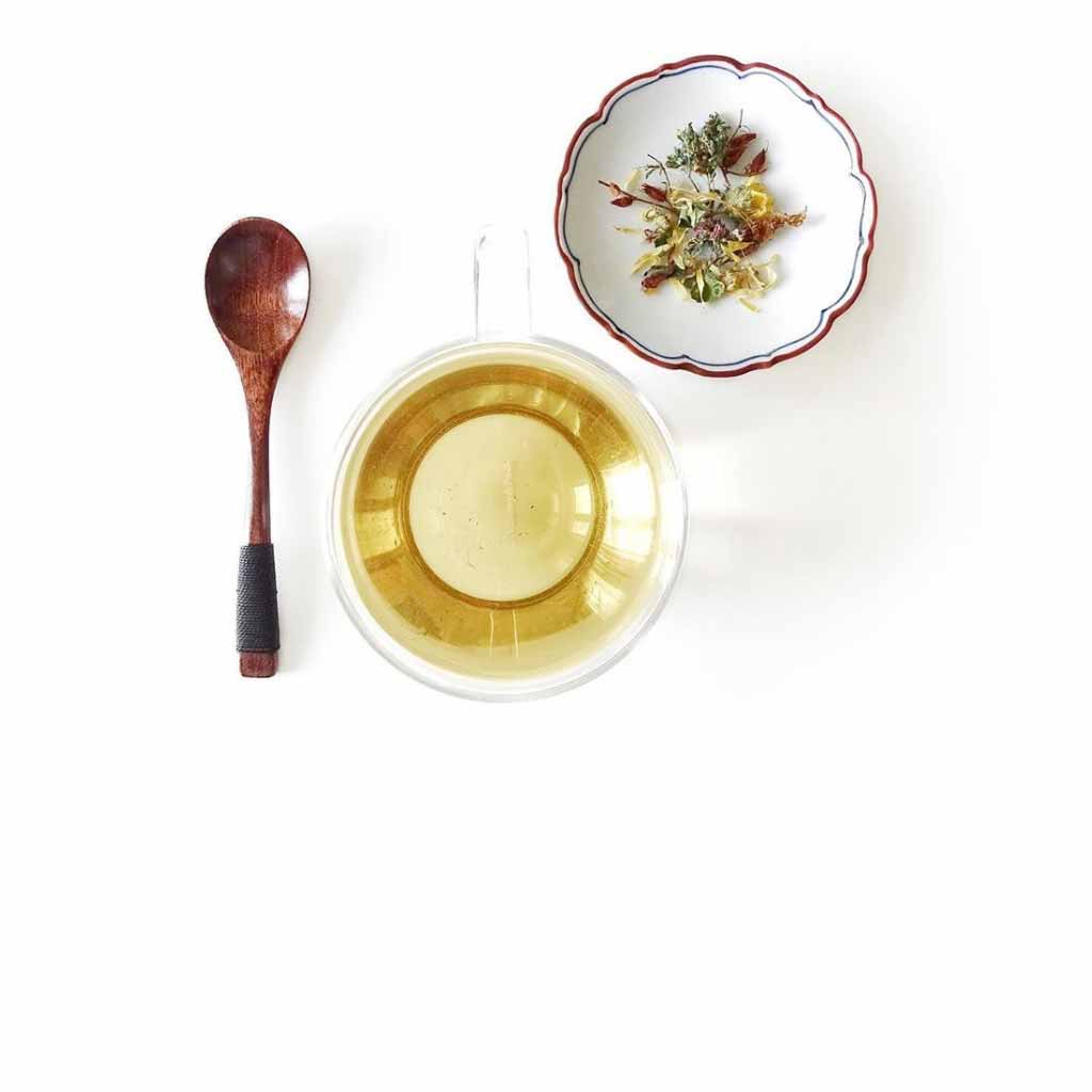 Cup with Health from Europe Organic Sunset Tea, wooden spoon and small bowl with dried herbs - lavender, chamomile, lemon balm