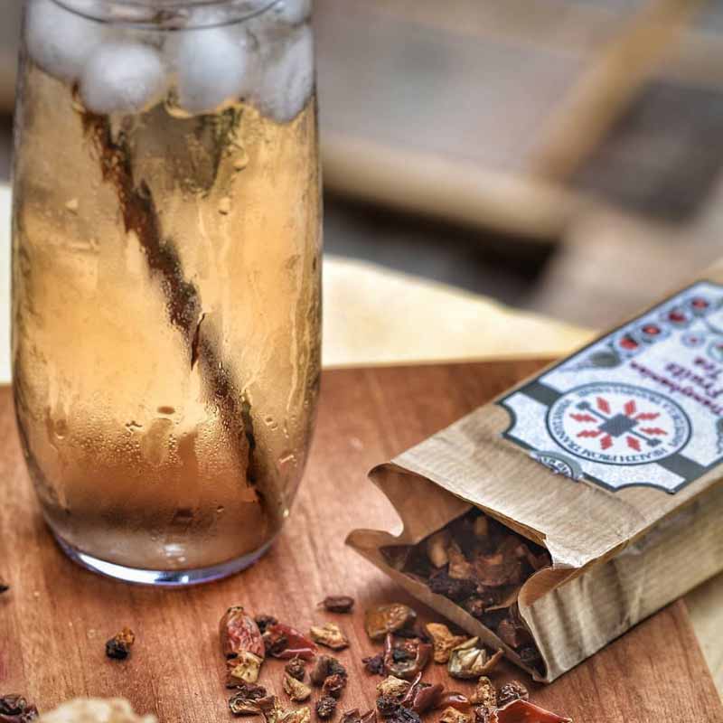 Glass of iced tea near open pack of Health from Europe Organic Fruits Tea and dried fruits on wooden board
