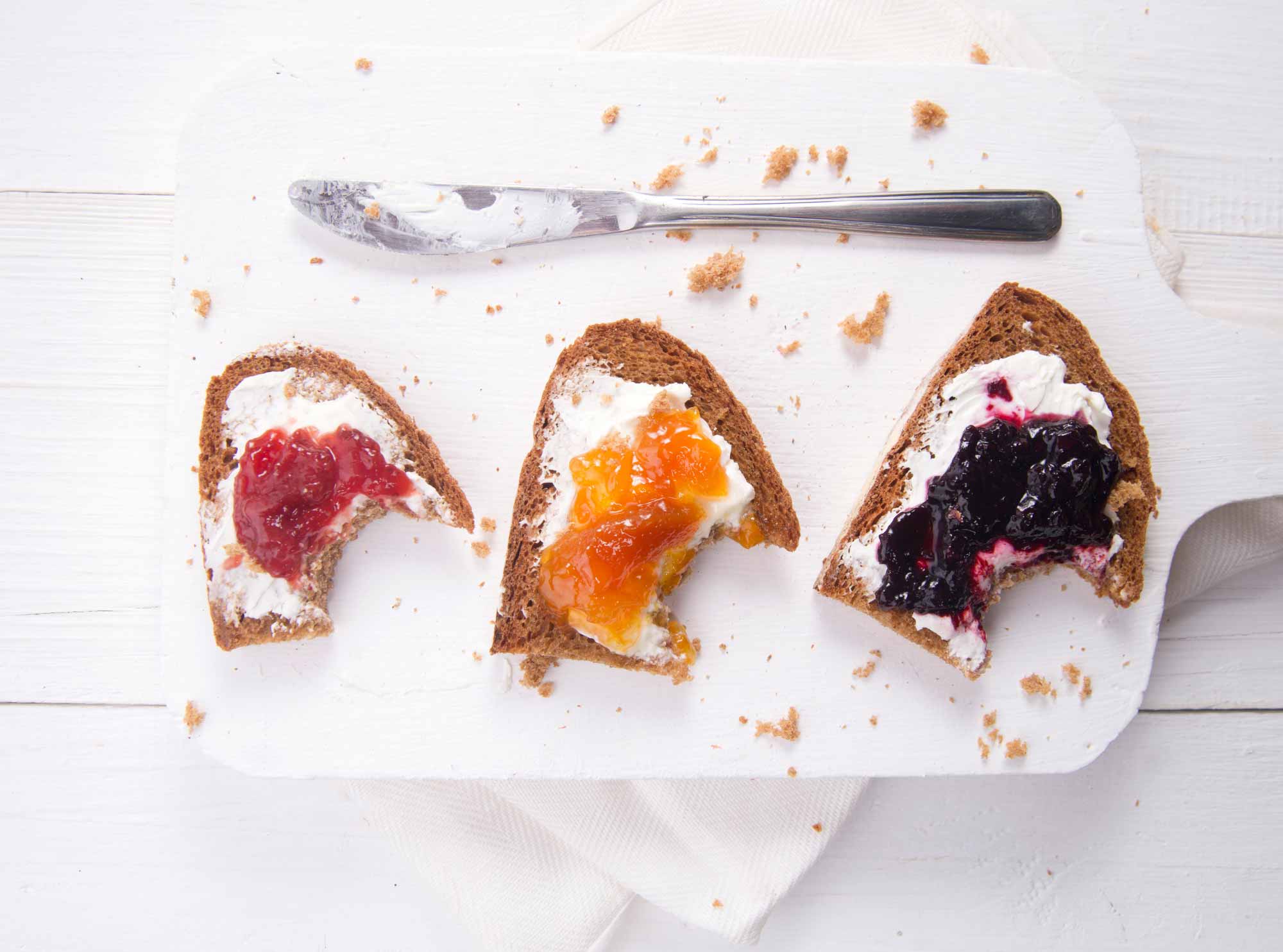 Three bitten slices of bread spread with rosehip jam, apricot jam and bilberry jam