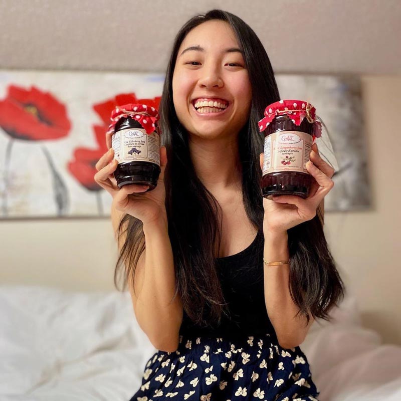 Young woman smiling and holding two Health from Europe jam jars - elderberry and rosehip